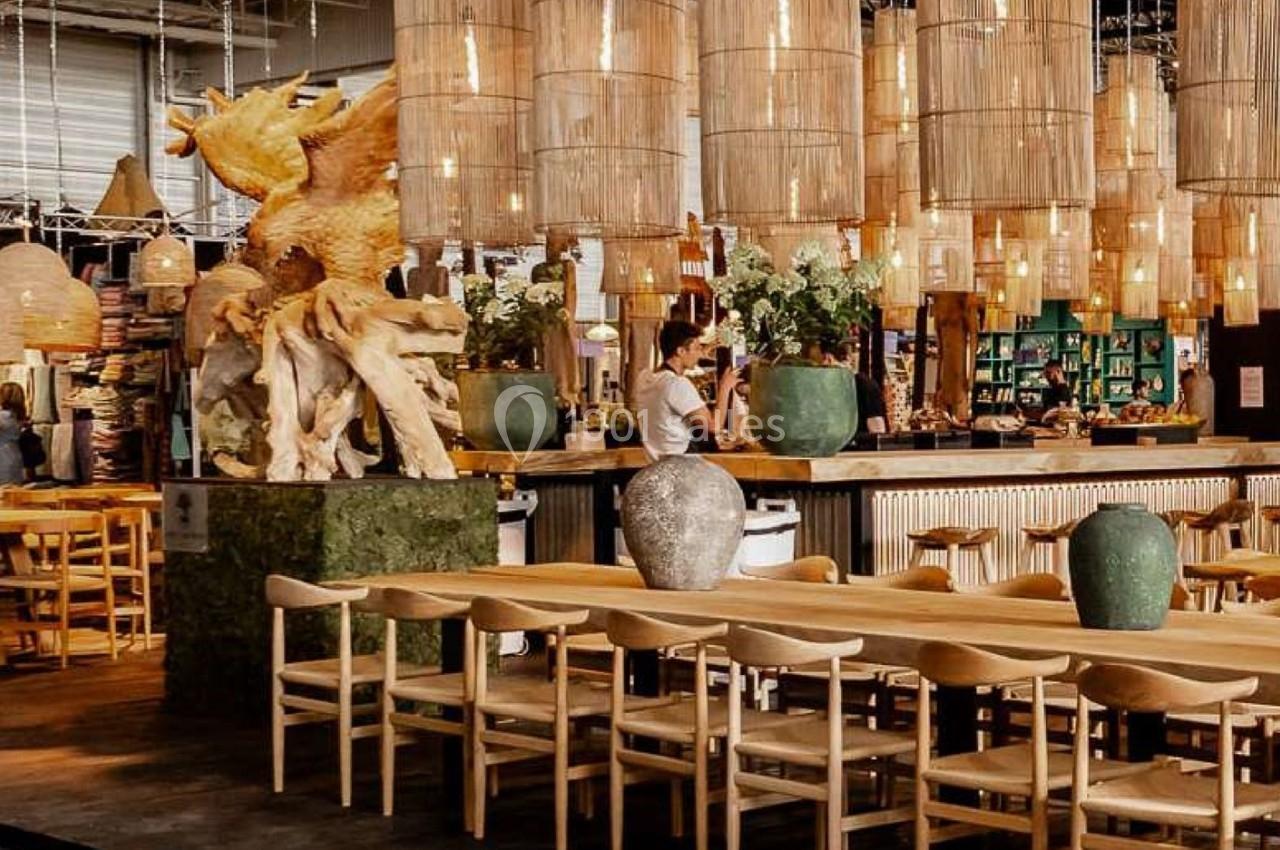 Salle de restaurant avec tables en bois, chaises assorties, sculptures et suspensions lumineuses en osier.