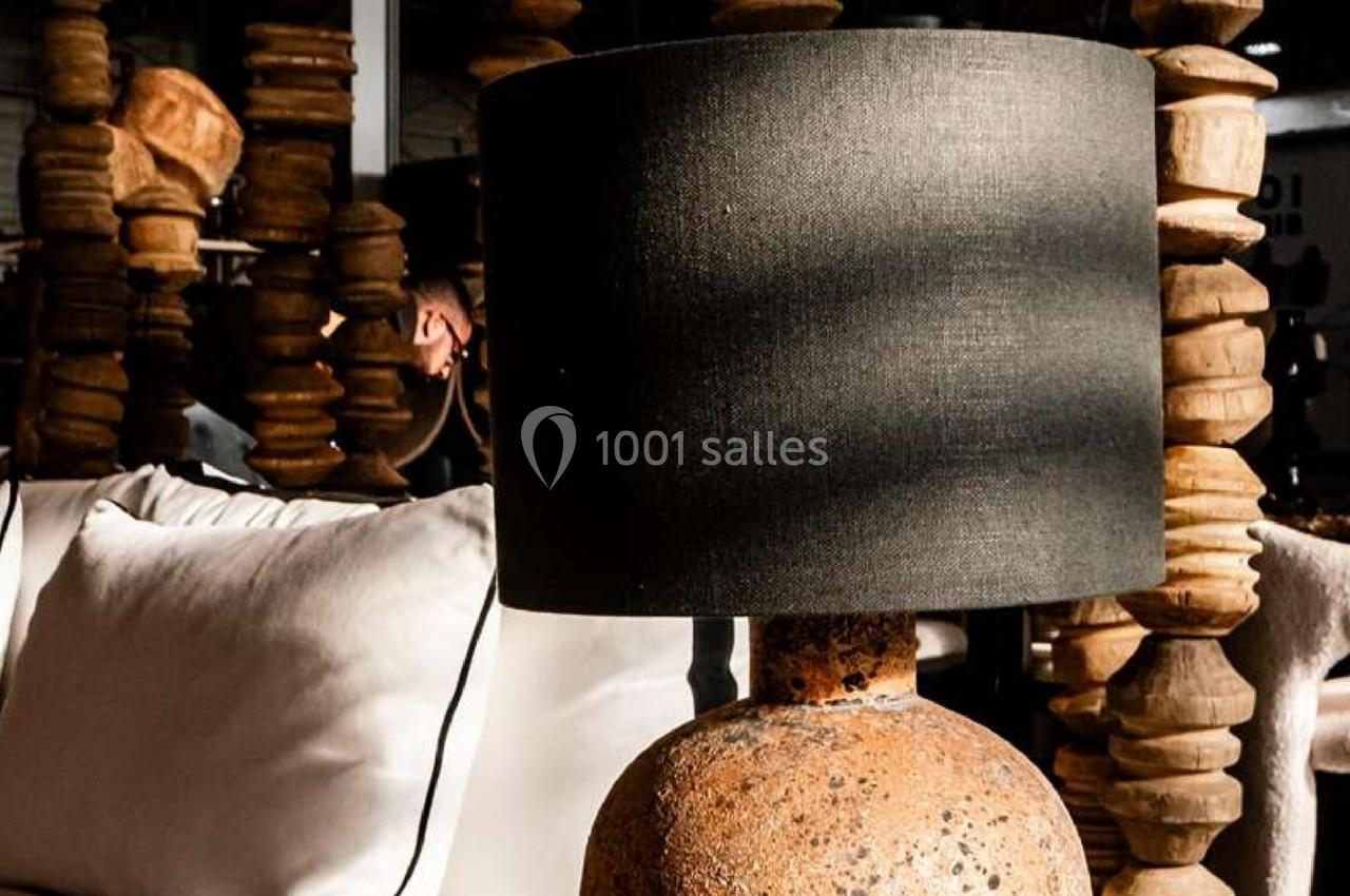 Lampe à abat-jour noir sur pied en pierre texturée, posée devant un canapé blanc dans un décor en bois sculpté.