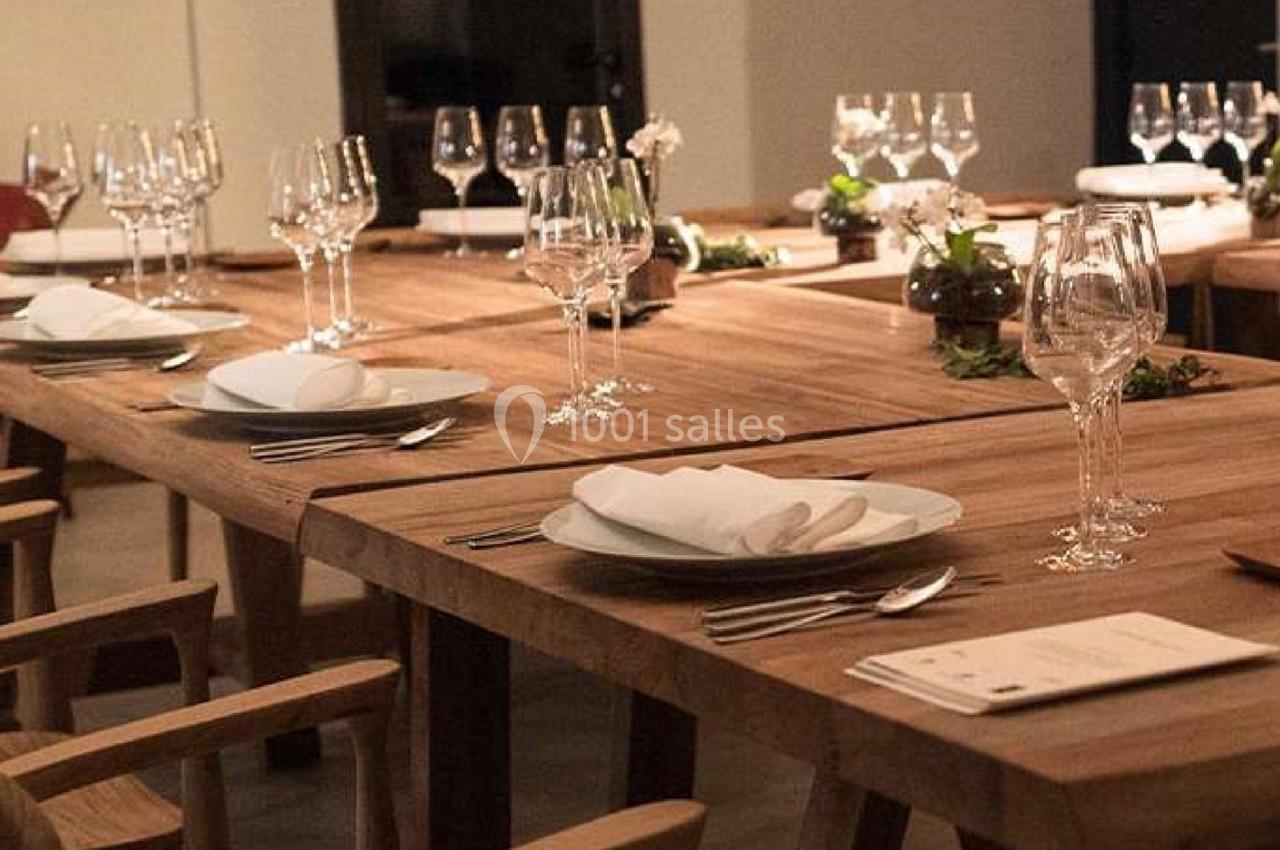 Tables en bois dressées avec des assiettes, des verres et des serviettes blanches dans une salle élégante.