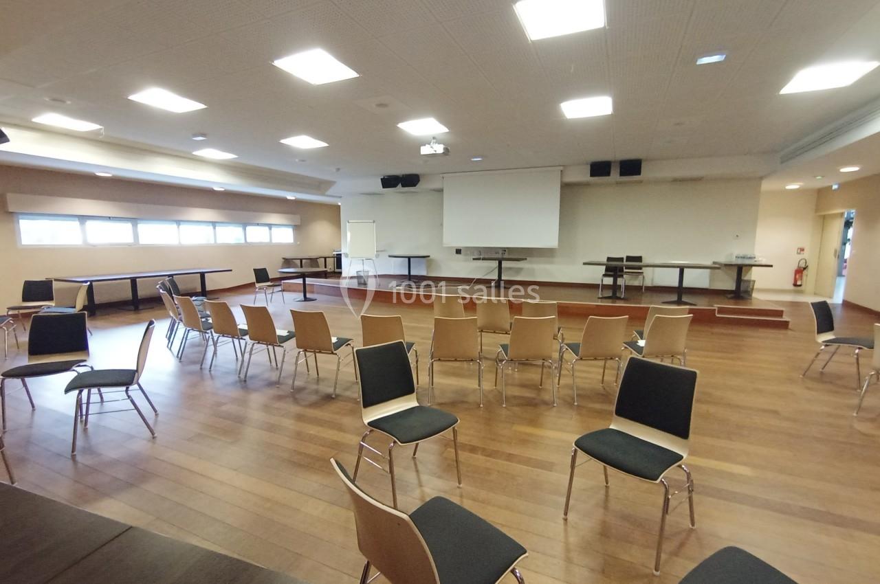 Salle de conférence lumineuse avec des chaises disposées en cercle, un écran de projection et une estrade en bois.