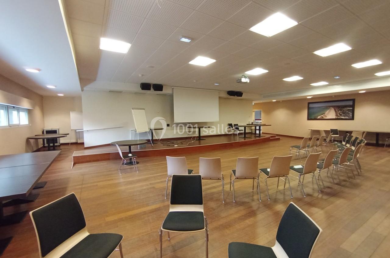 Salle de conférence avec chaises disposées face à un écran de projection, tableau blanc et tables en arrière-plan.