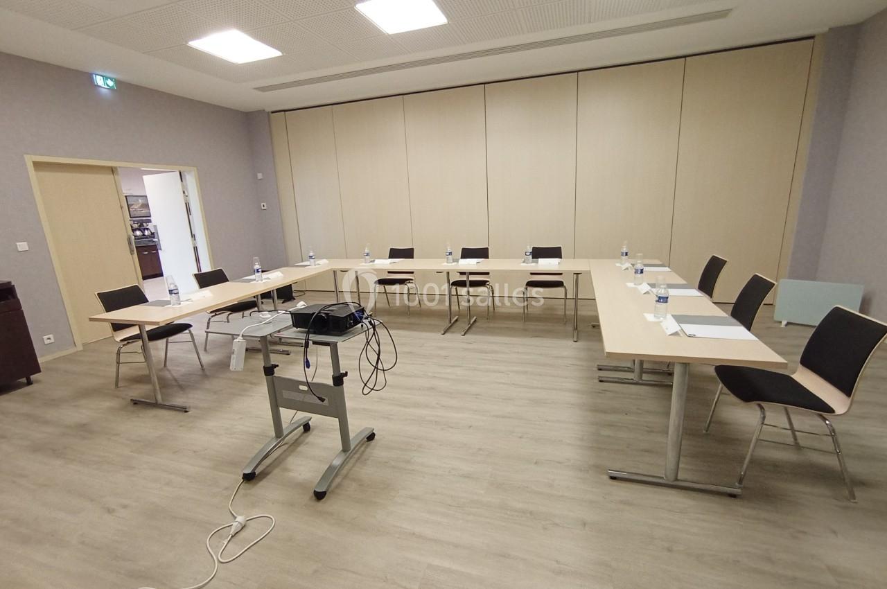 Salle de réunion équipée de tables disposées en U, chaises, bouteilles d'eau et matériel de projection.
