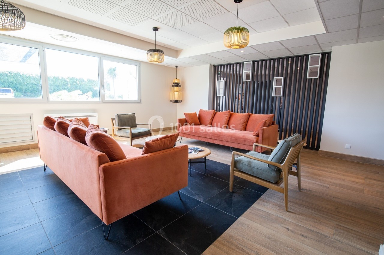 Salon moderne avec canapés orange, fauteuils en bois, sol en carrelage et parquet, et grande fenêtre lumineuse.