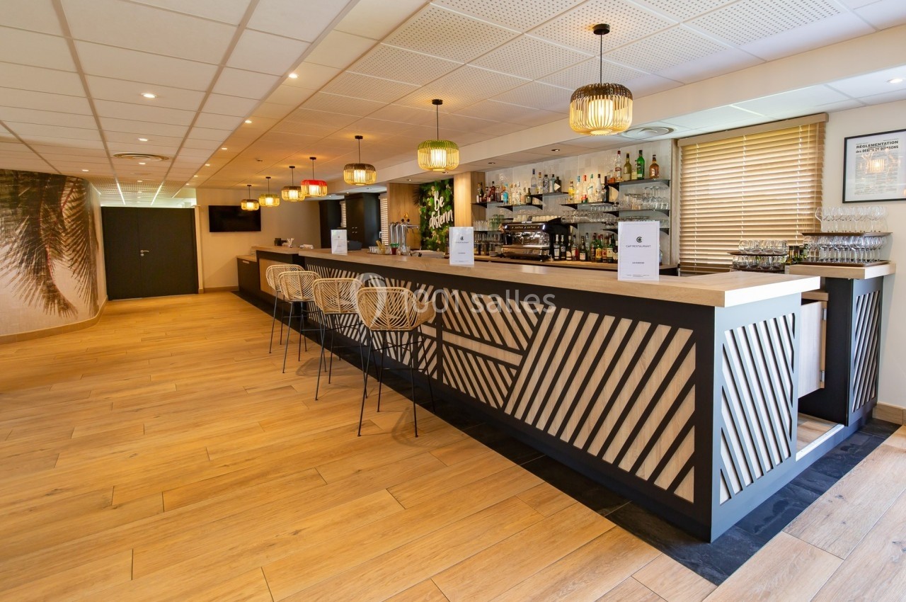 Bar moderne avec comptoir en bois et métal, tabourets design, étagères garnies de bouteilles et éclairage suspendu.