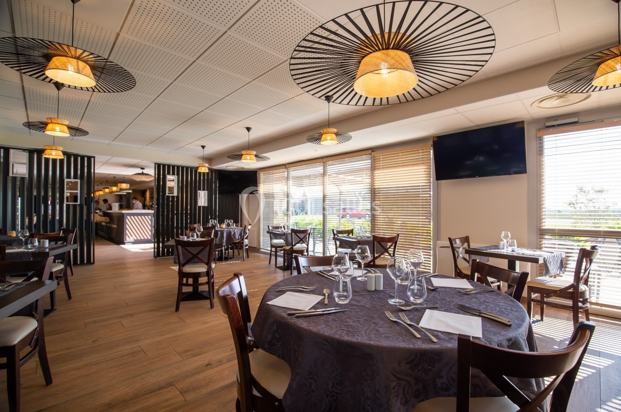 Salle de restaurant lumineuse avec tables dressées, grandes baies vitrées et décoration moderne.