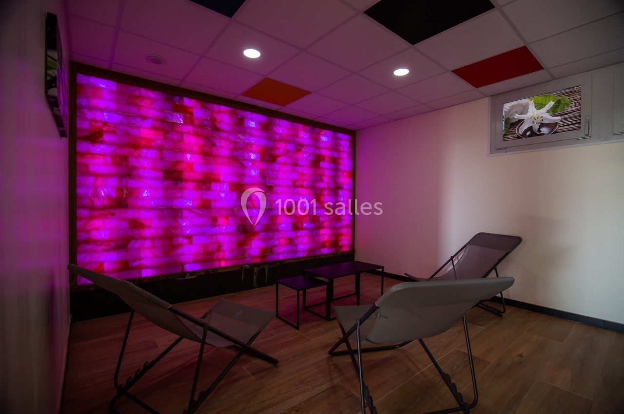 Salle de détente avec mur lumineux rose, chaises longues grises et sol en bois clair.