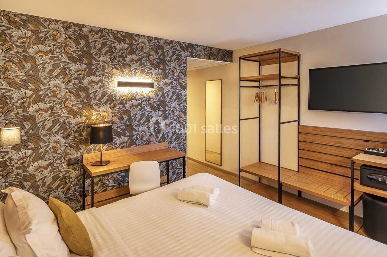 Chambre d'hôtel avec lit double, bureau en bois, télévision murale, penderie ouverte et éclairage moderne.