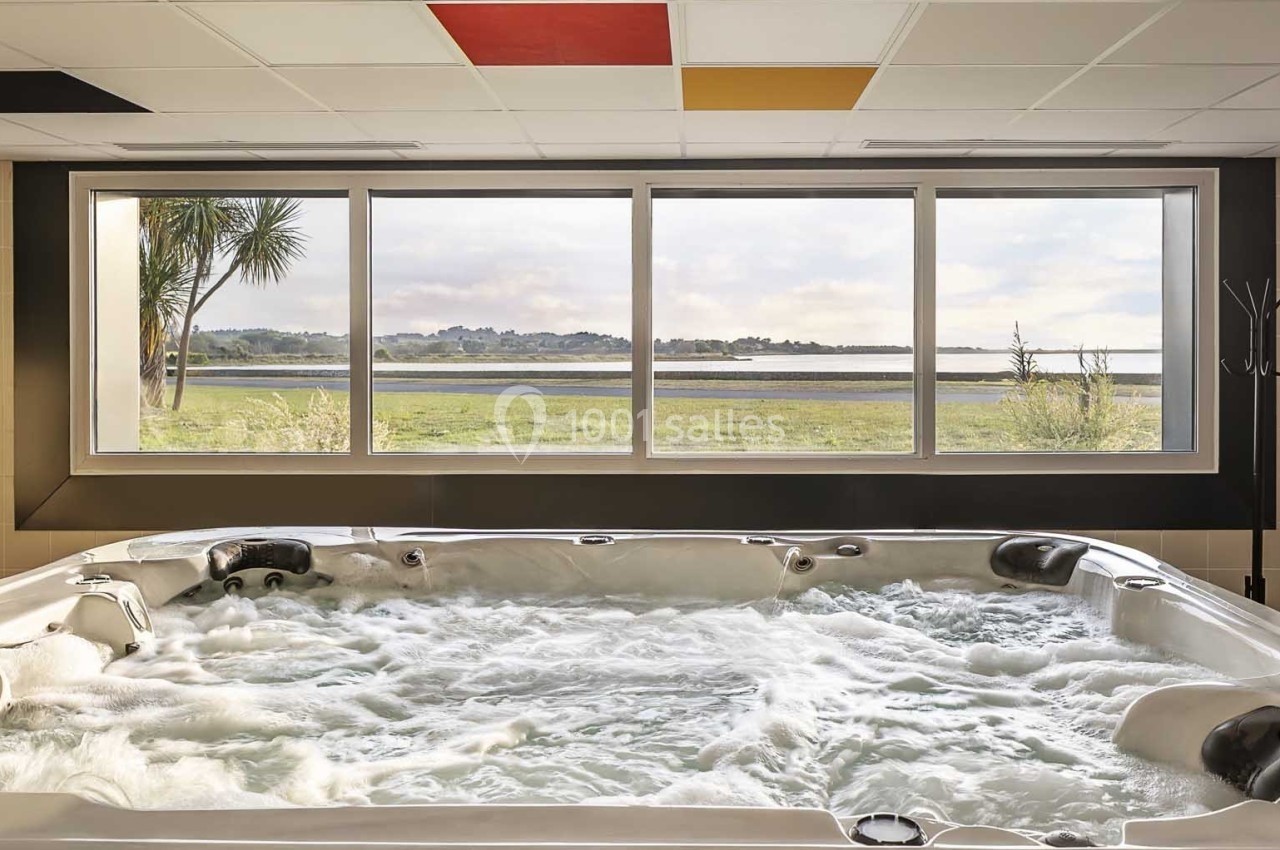 Bain à remous intérieur avec vue sur un paysage naturel à travers une grande baie vitrée.