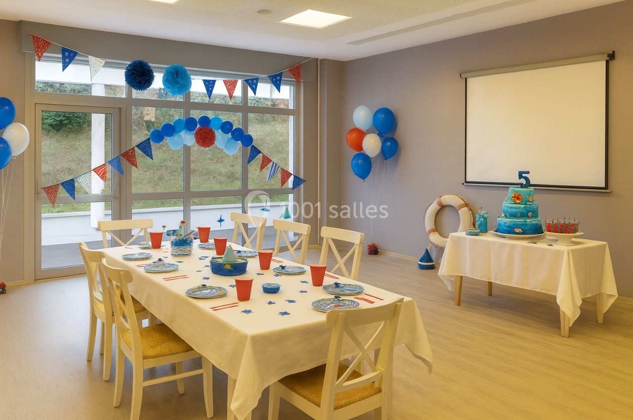 Salle décorée pour une fête d'anniversaire avec table dressée, ballons, guirlandes et gâteau sur une table annexe.