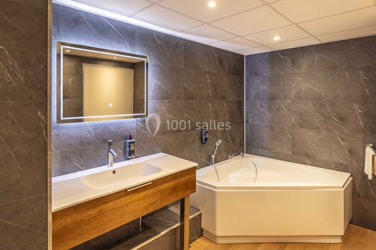 Salle de bain moderne avec un lavabo en bois, un miroir éclairé et une baignoire d'angle sur un sol en bois.