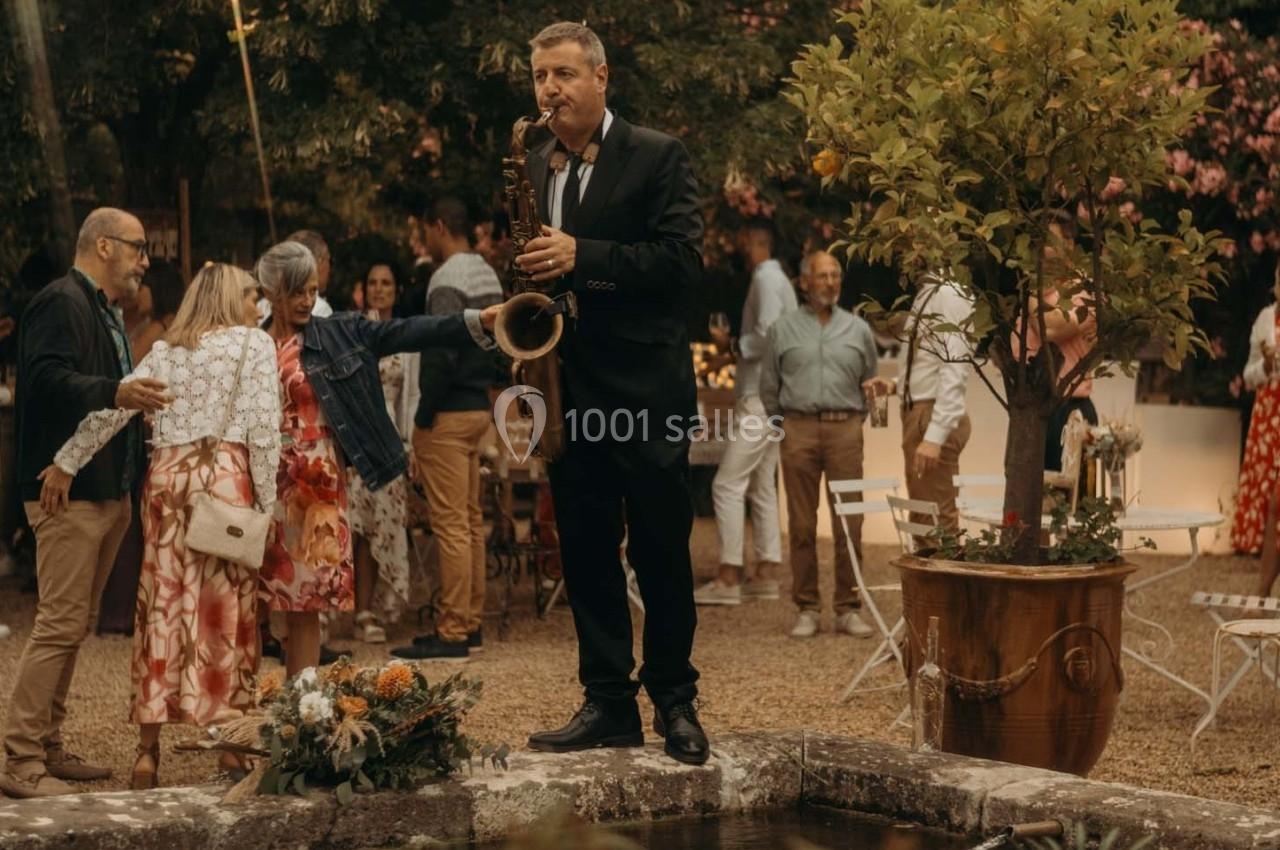 Un musicien joue du saxophone en extérieur lors d'un événement, entouré d'invités dans une ambiance conviviale.