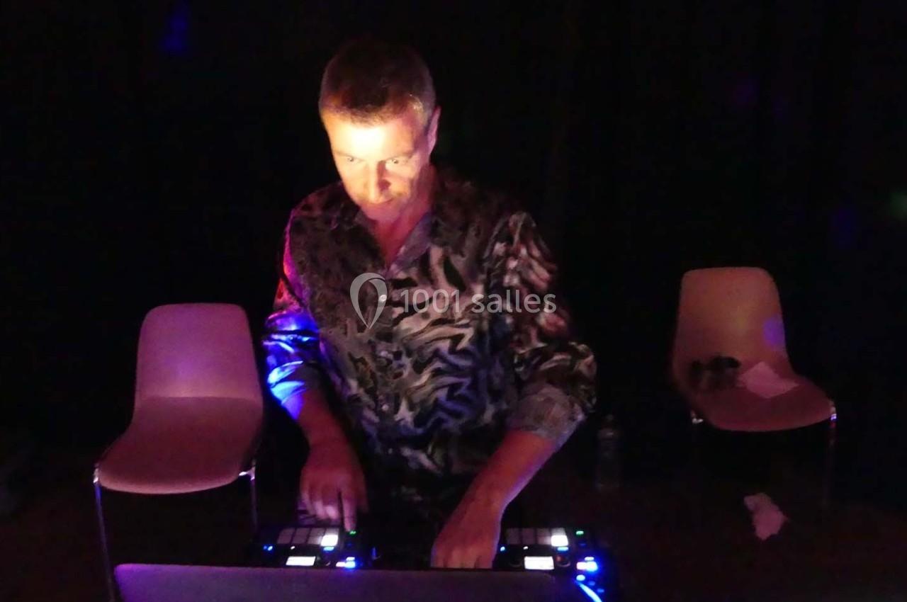Un DJ mixe de la musique sur une console lumineuse dans une pièce sombre avec des chaises en arrière-plan.