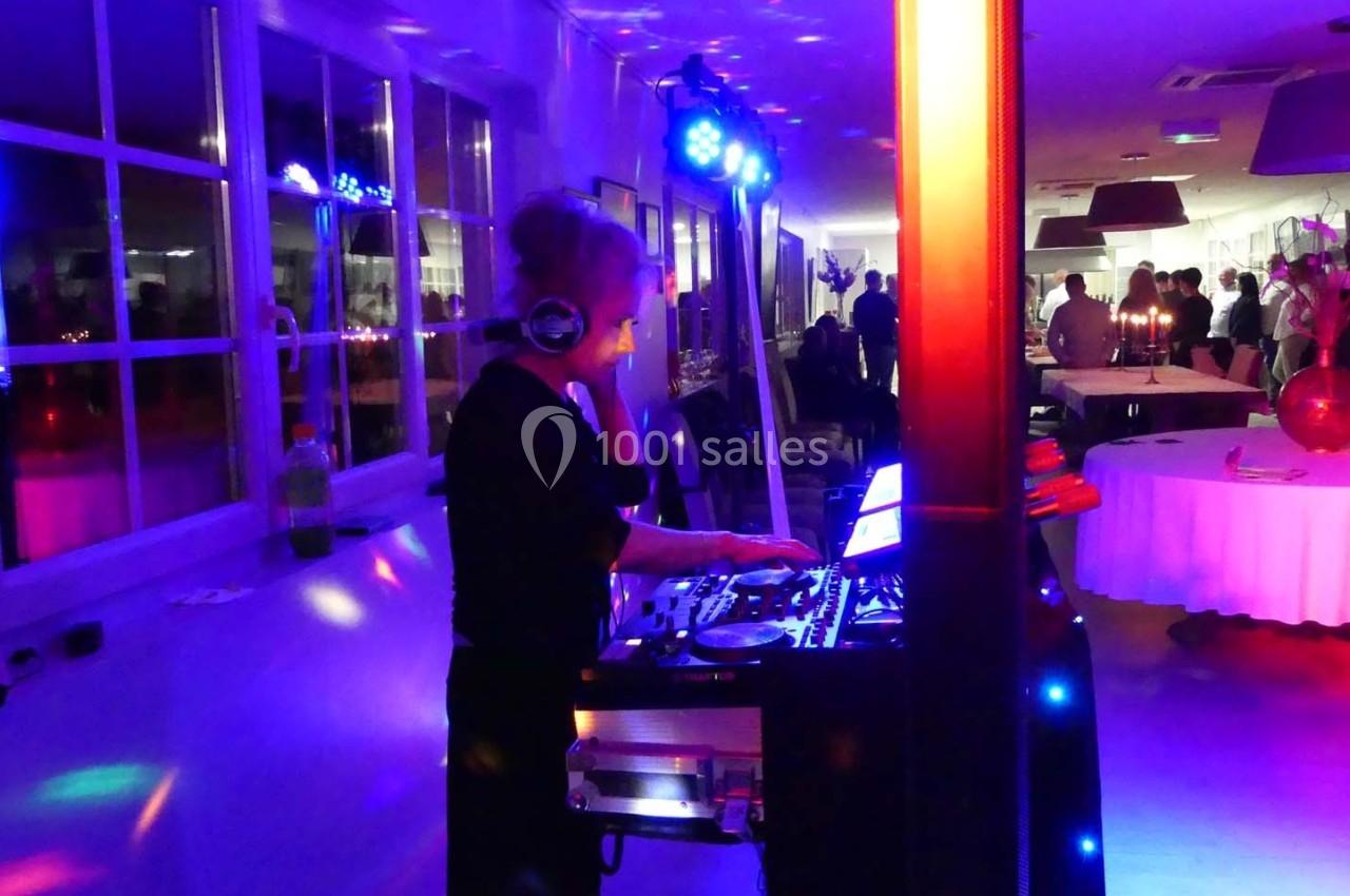 Une DJ anime une soirée dans une salle éclairée par des lumières colorées, avec des invités en arrière-plan.