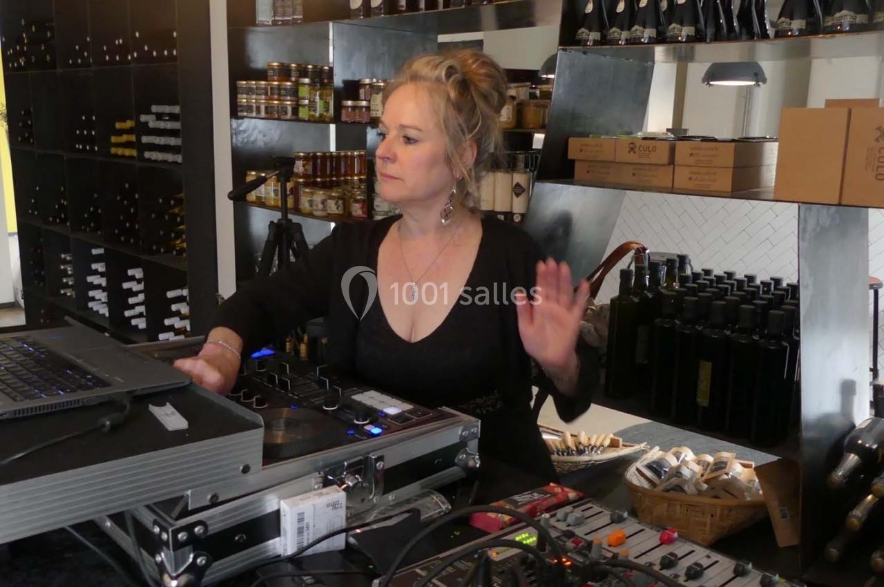 Femme utilisant un équipement de mixage audio dans un magasin avec des étagères remplies de bouteilles et de produits.