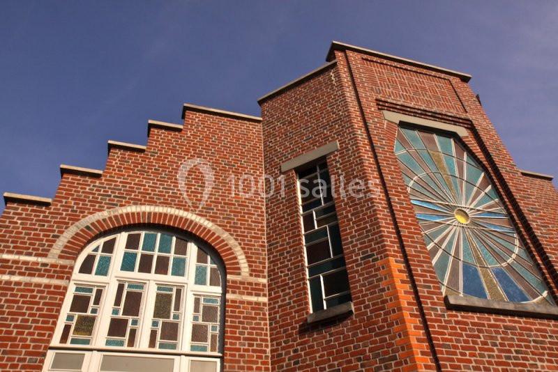 Location salle Comines (Nord) - Les Salons du Château - France Evénement #15 Façade en briques rouges avec des fenêtres en vitraux colorés et un motif en éventail sous un ciel bleu.