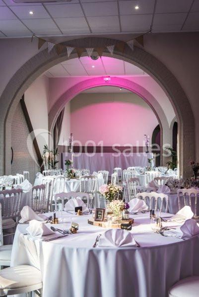 Location salle Comines (Nord) - Les Salons du Château - France Evénement #12 Salle de réception décorée avec des tables rondes, nappes blanches, chaises assorties et éclairage rose tamisé.