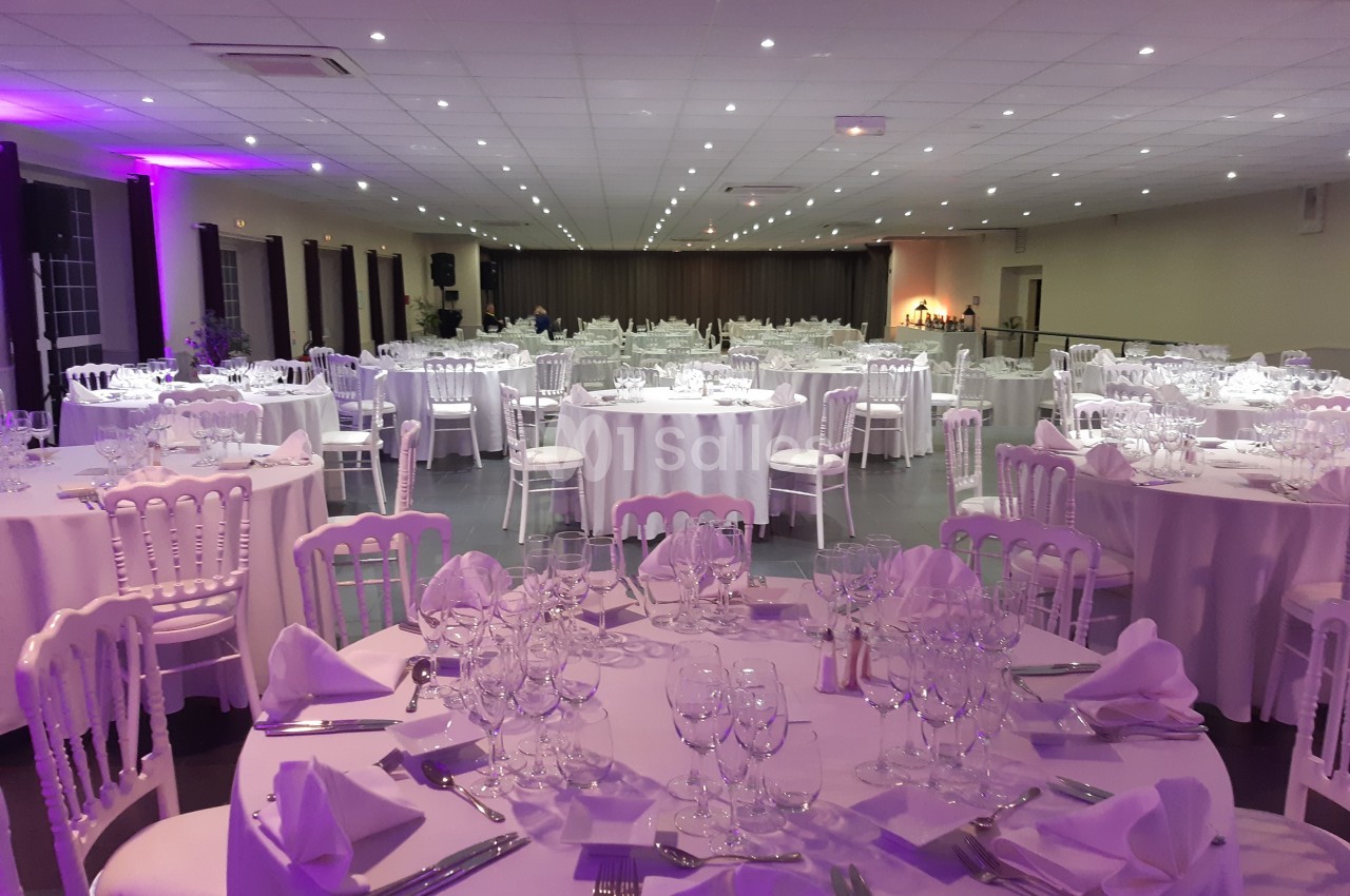 Salle de réception décorée avec des tables rondes dressées de nappes blanches, verres et couverts.