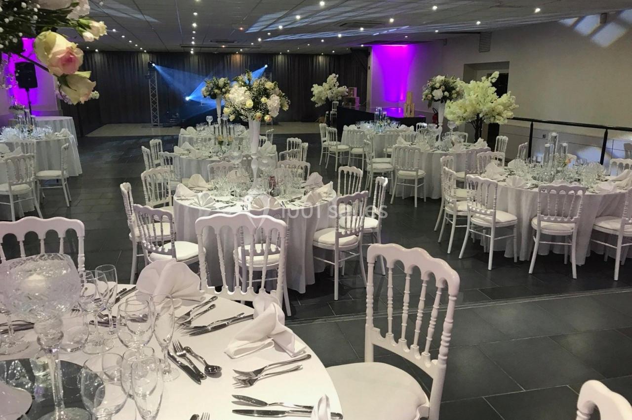 Location salle Comines (Nord) - Les Salons du Château - France Evénement #29 Salle de réception élégamment décorée avec des tables rondes, nappes blanches, chaises assorties et éclairage coloré.