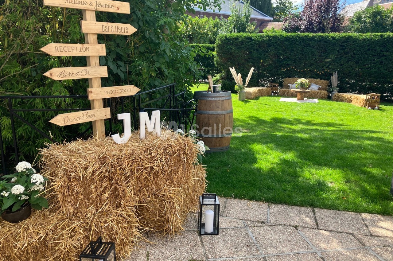 Panneaux en bois indiquant des directions dans un jardin décoré avec des bottes de paille, lanternes et tonneau.
