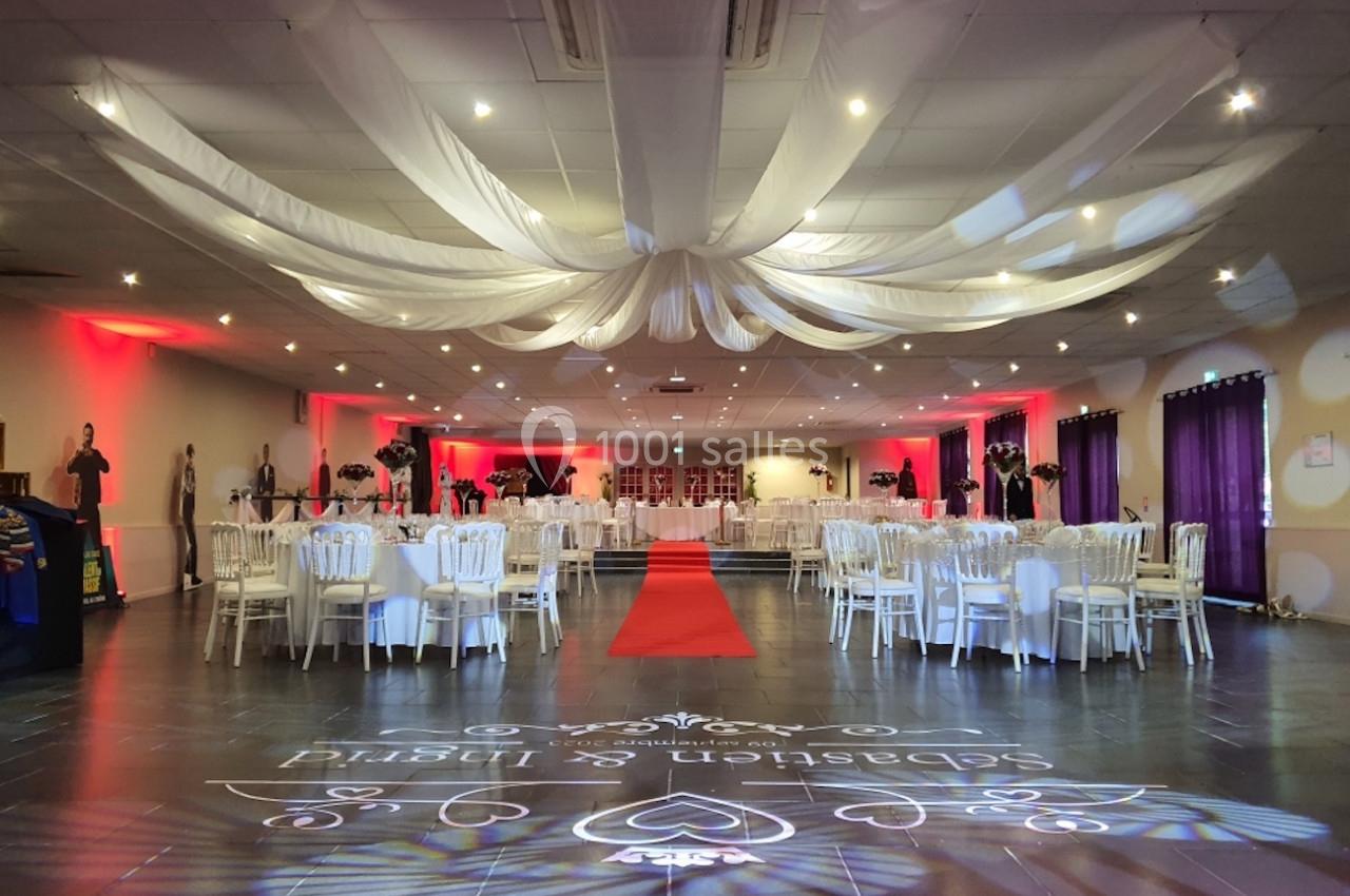 Location salle Comines (Nord) - Les Salons du Château - France Evénement #6 Salle de réception décorée avec des tables rondes, des chaises blanches, un tapis rouge et un plafond drapé de tissu blanc.