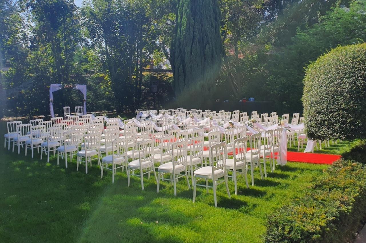 Location salle Comines (Nord) - Les Salons du Château - France Evénement #32 Chaises blanches alignées en extérieur pour une cérémonie, entourées de verdure et éclairées par le soleil.