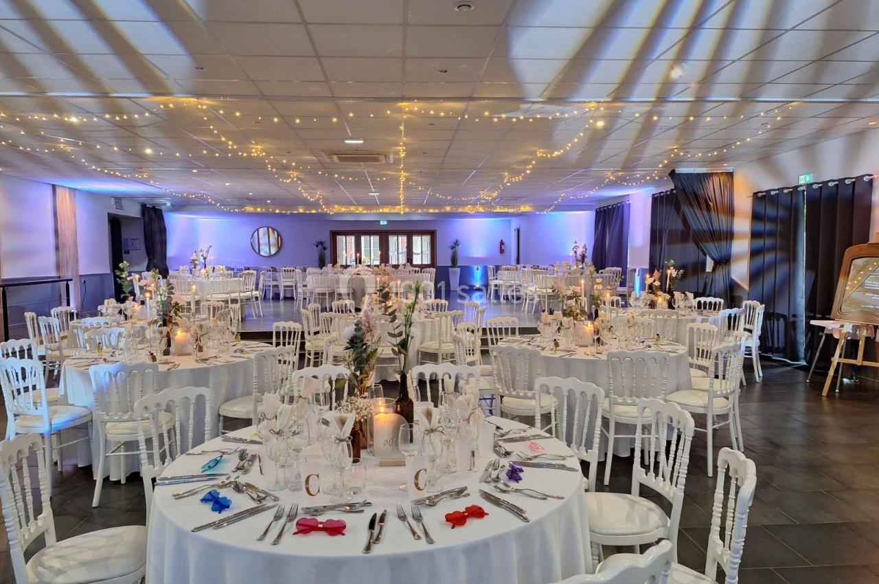 Location salle Comines (Nord) - Les Salons du Château - France Evénement #4 Salle de réception décorée avec des tables rondes dressées, chaises blanches et guirlandes lumineuses suspendues.