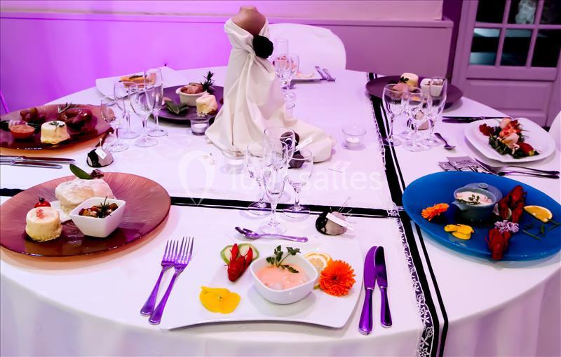 Location salle Comines (Nord) - Les Salons du Château - France Evénement #11 Table dressée avec des assiettes gastronomiques colorées, couverts disposés et décoration élégante sous éclairage violet.