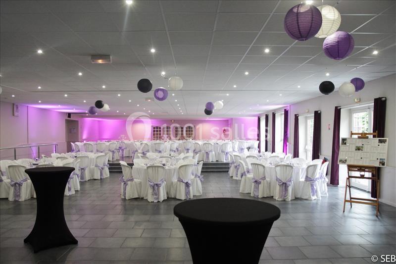 Location salle Comines (Nord) - Les Salons du Château - France Evénement #7 Salle de réception décorée avec des tables rondes, nappes blanches, nœuds violets et lanternes suspendues.