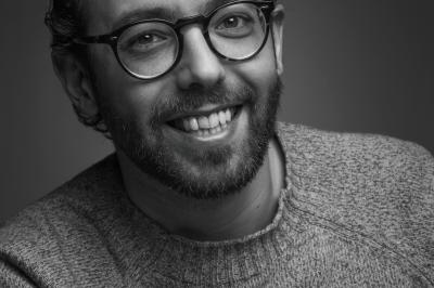 Miniature Yann Cœuru Photographie #1 Femme assise, vêtue d'une robe blanche fluide, posant avec une expression sereine sur fond neutre.