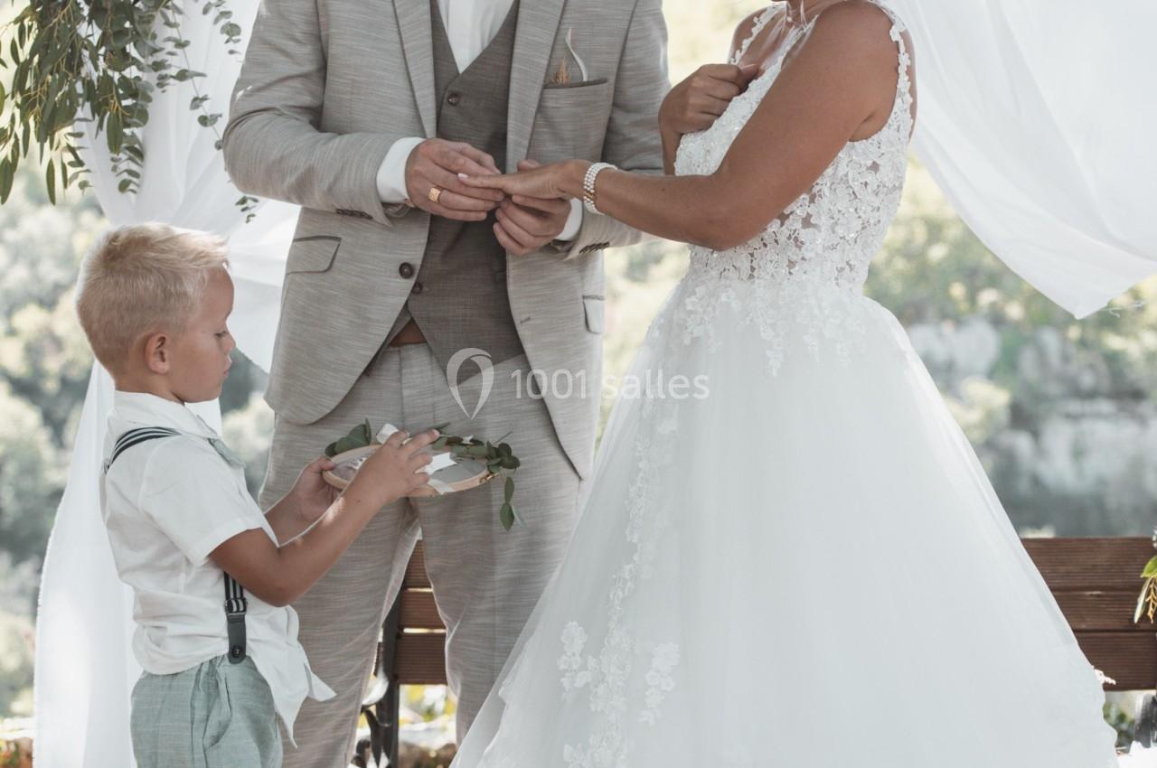 Un couple échange des alliances lors d'une cérémonie de mariage en extérieur, accompagné d'un enfant tenant un coussin.