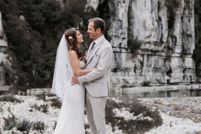 Miniature Elodie & David Femme assise, vêtue d'une robe blanche fluide, posant avec une expression sereine sur fond neutre.