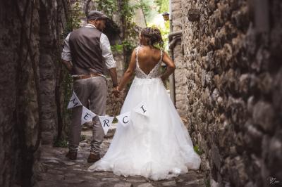 Miniature Labeaume - Mairage Corinne & Romain Femme assise, vêtue d'une robe blanche fluide, posant avec une expression sereine sur fond neutre.