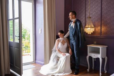 Miniature Mariage Alès Femme assise, vêtue d'une robe blanche fluide, posant avec une expression sereine sur fond neutre.