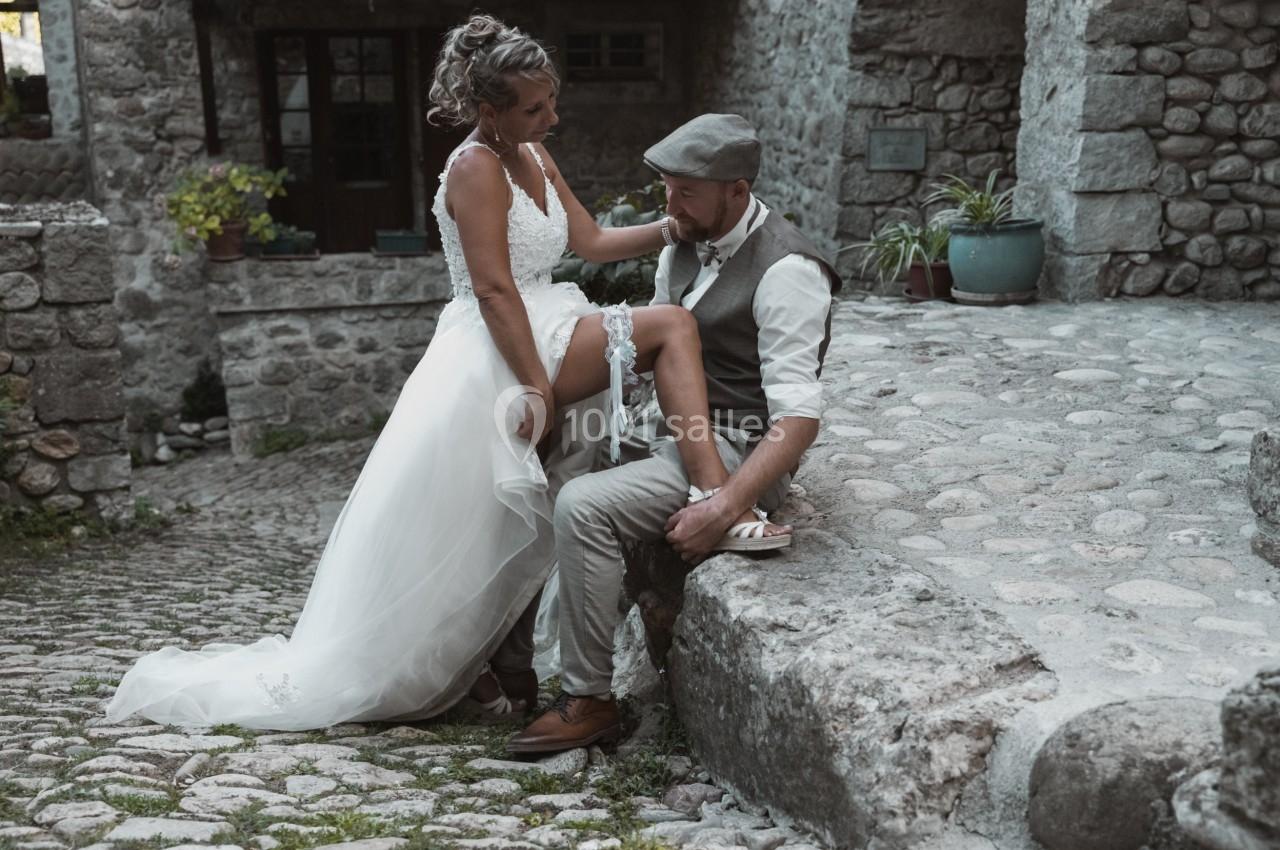 Une mariée ajuste sa jarretière en posant sa jambe sur un genou de son partenaire dans une ruelle pavée.