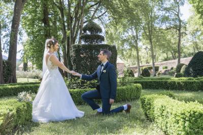 Miniature Mariage Myriam & Romain Femme assise, vêtue d'une robe blanche fluide, posant avec une expression sereine sur fond neutre.