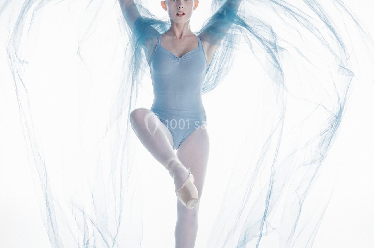 Danseuse en tenue bleue sur pointes, entourée de voiles transparents formant des courbes aériennes.