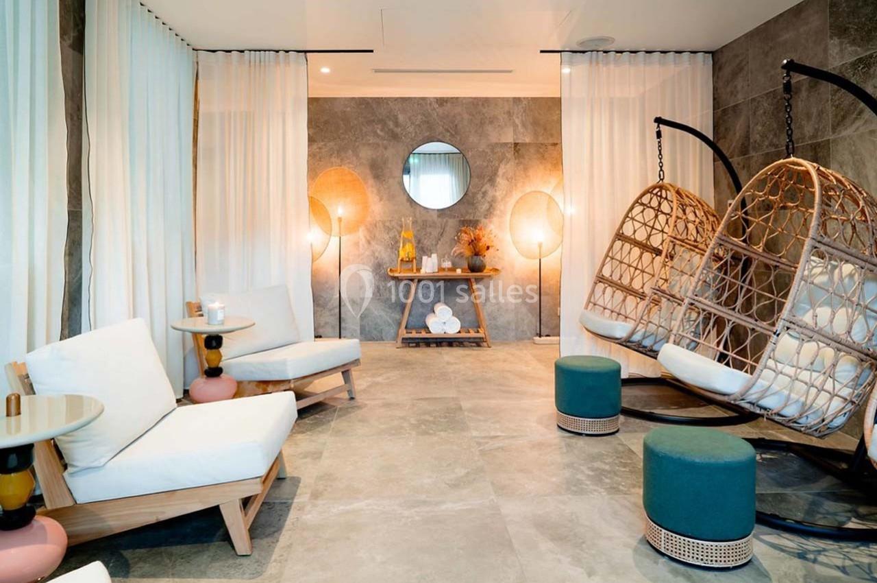 Espace détente avec fauteuils suspendus, chaises rembourrées, tables basses et éclairage doux dans une pièce moderne.