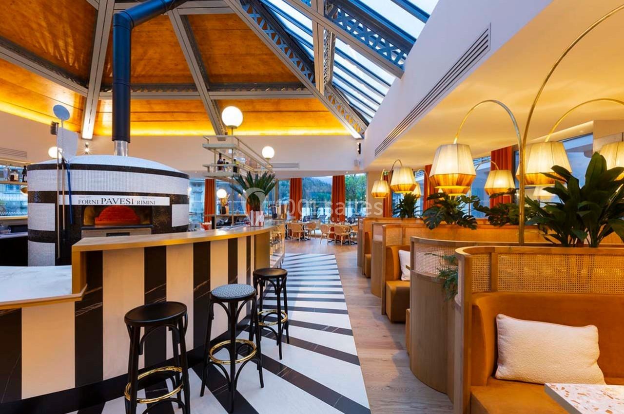 Intérieur d'un restaurant lumineux avec un four à pizza, des banquettes en cuir et un toit en verre.