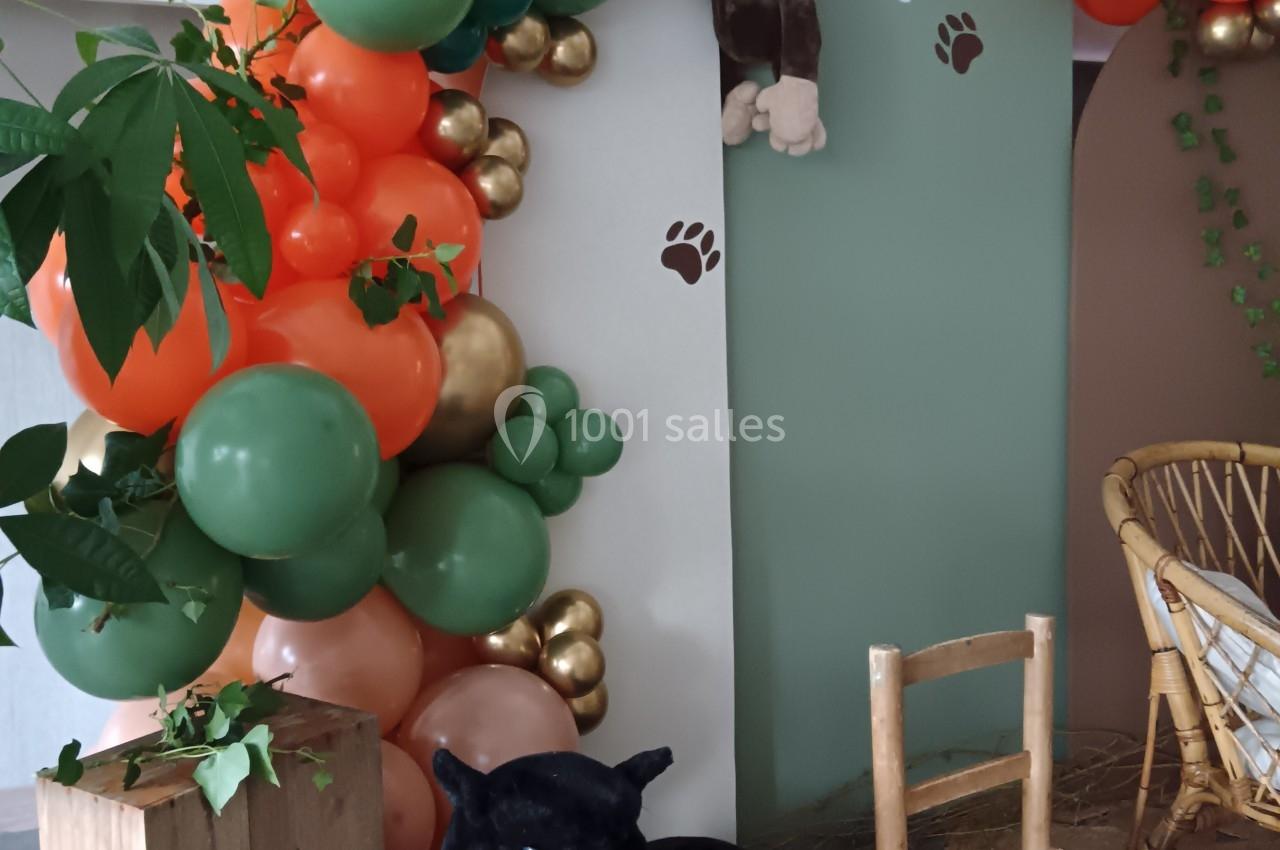 Décoration de baptême avec arche de ballons verts, orange et dorés, peluche de singe suspendue et panthère noire en peluche.