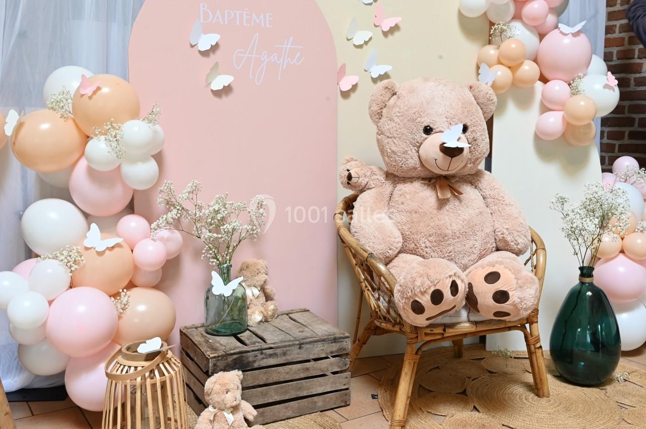 Décoration de baptême avec ours en peluche, ballons pastel, fleurs et papillons en papier dans un cadre chaleureux.