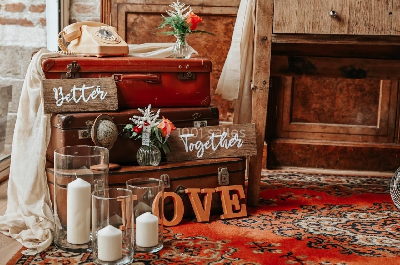 Empilement de valises vintage avec des décorations florales, des bougies et des panneaux en bois portant des messages…