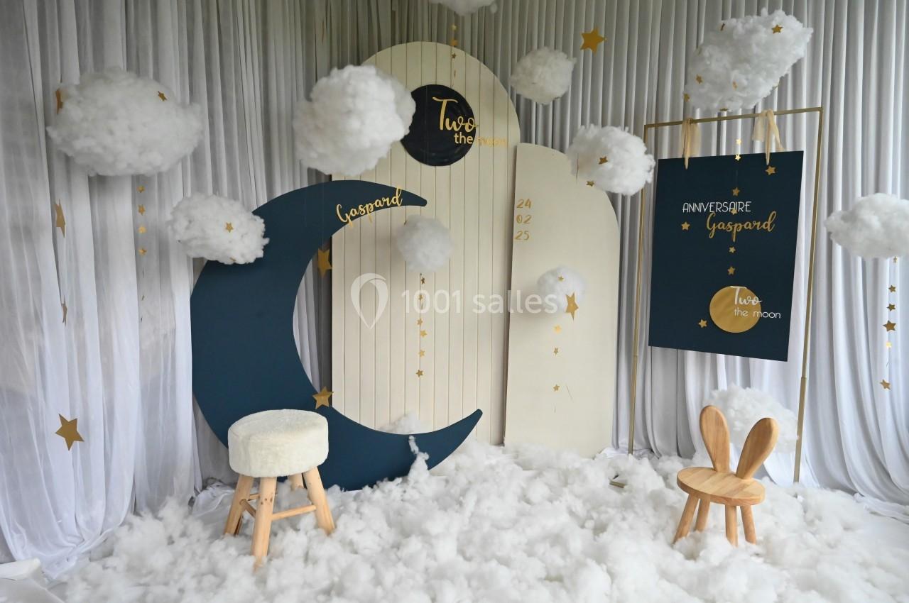 Décor sur le thème de la lune avec des nuages suspendus, des étoiles dorées et des chaises en bois.