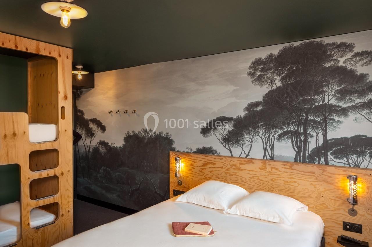 Chambre avec lit double, lits superposés en bois, éclairage chaleureux et mur décoré d'une fresque de paysage naturel.