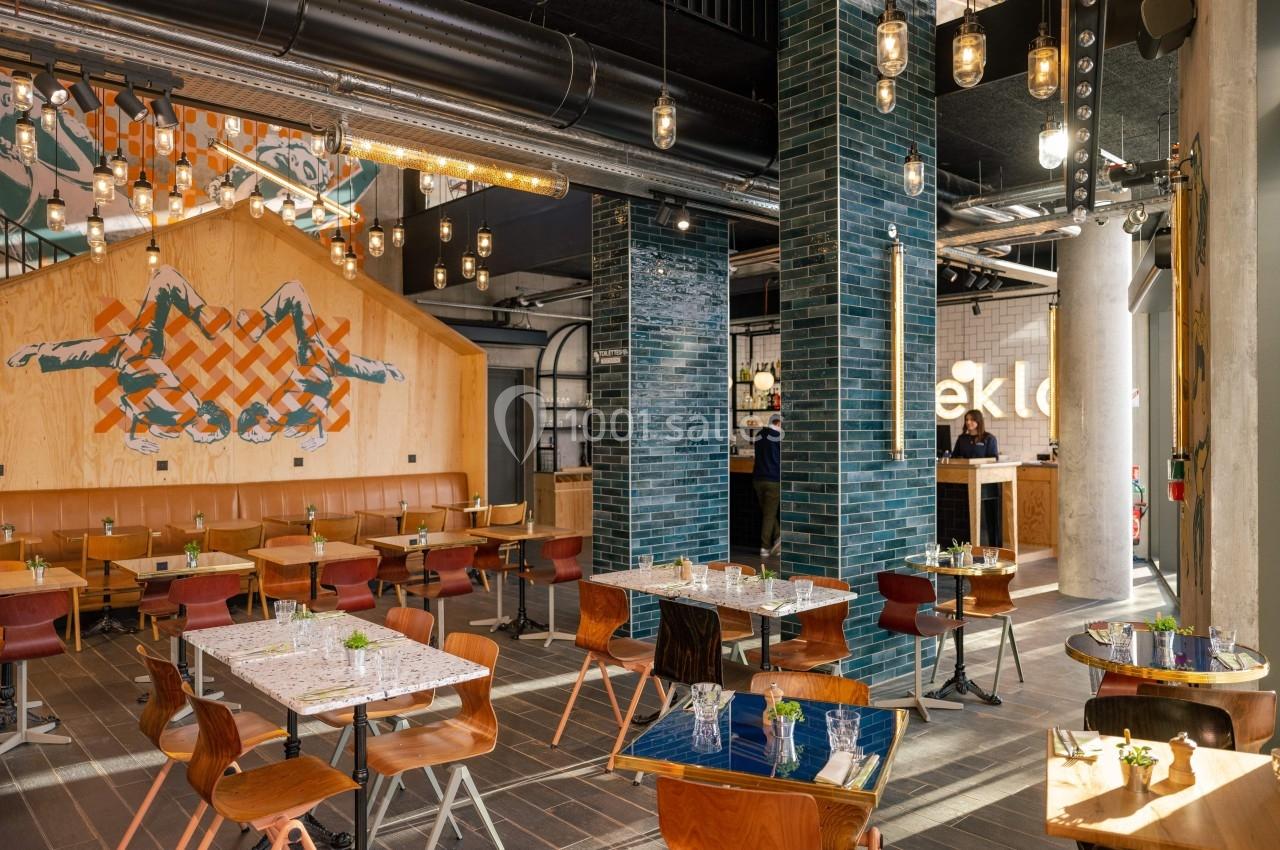 Salle de restaurant moderne avec tables en bois, décoration murale artistique et éclairage suspendu.