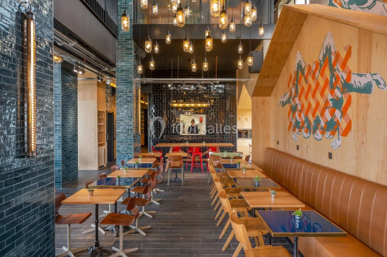 Salle de restaurant moderne avec tables en bois, chaises design, éclairage suspendu et mur décoré de motifs colorés.