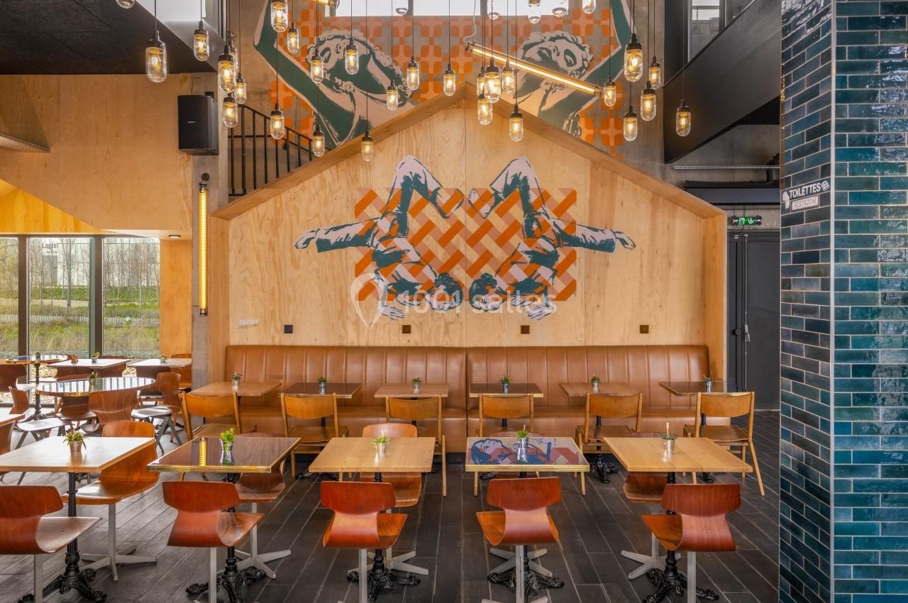 Salle de restaurant moderne avec tables en bois, chaises design, mur décoré d'une fresque et éclairage suspendu.