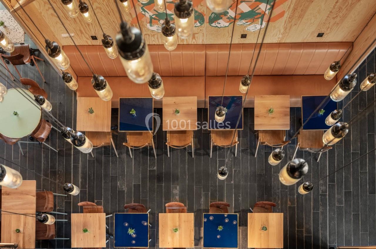 Vue plongeante sur une salle de restaurant avec des tables en bois, des chaises et un éclairage suspendu.