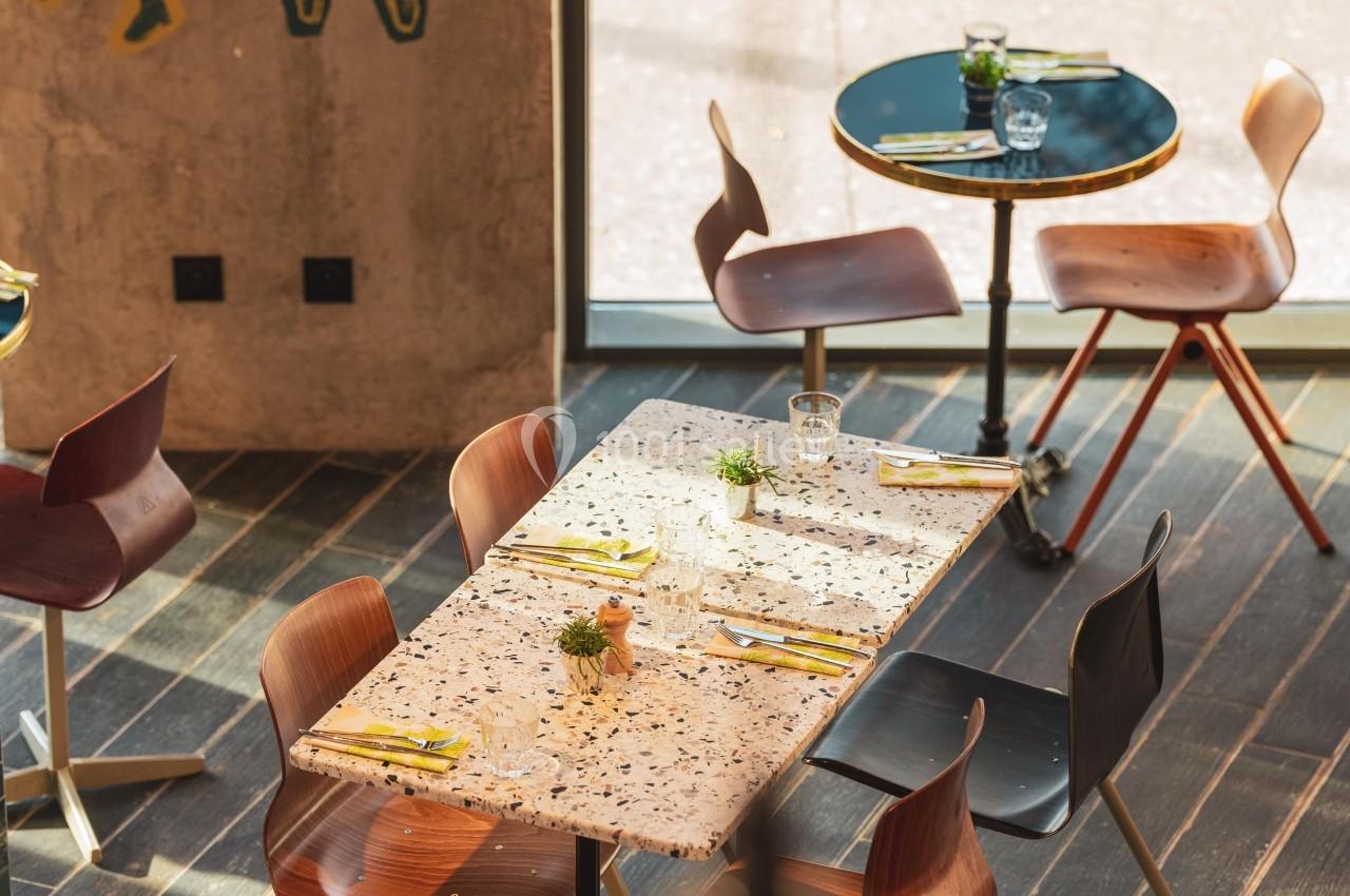 Salle de restaurant moderne avec tables dressées, chaises en bois et décoration murale artistique.
