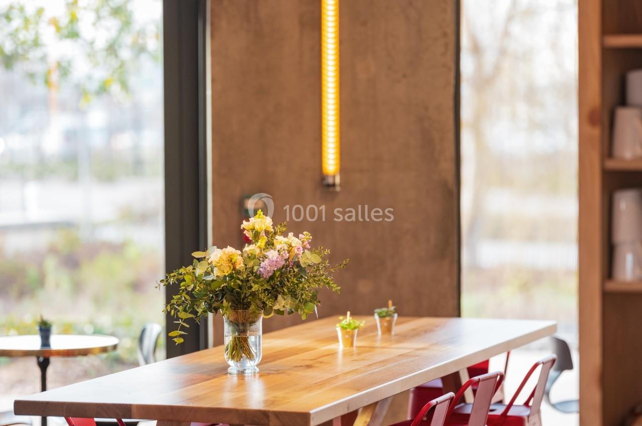 Table en bois entourée de chaises rouges, décorée avec un vase de fleurs, dans un intérieur lumineux et moderne.