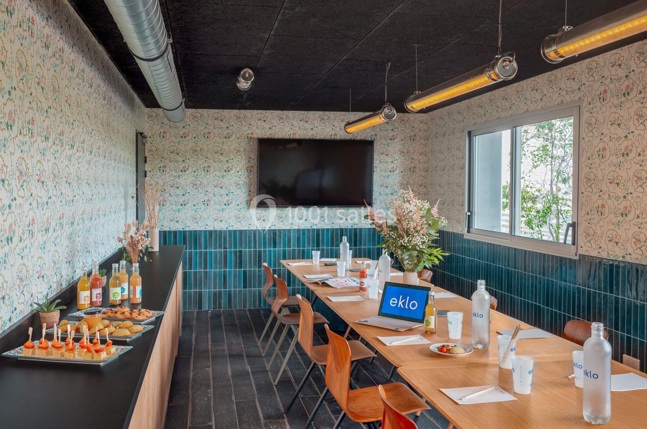 Salle de réunion lumineuse avec table en bois, chaises design, écran mural et buffet de collations.